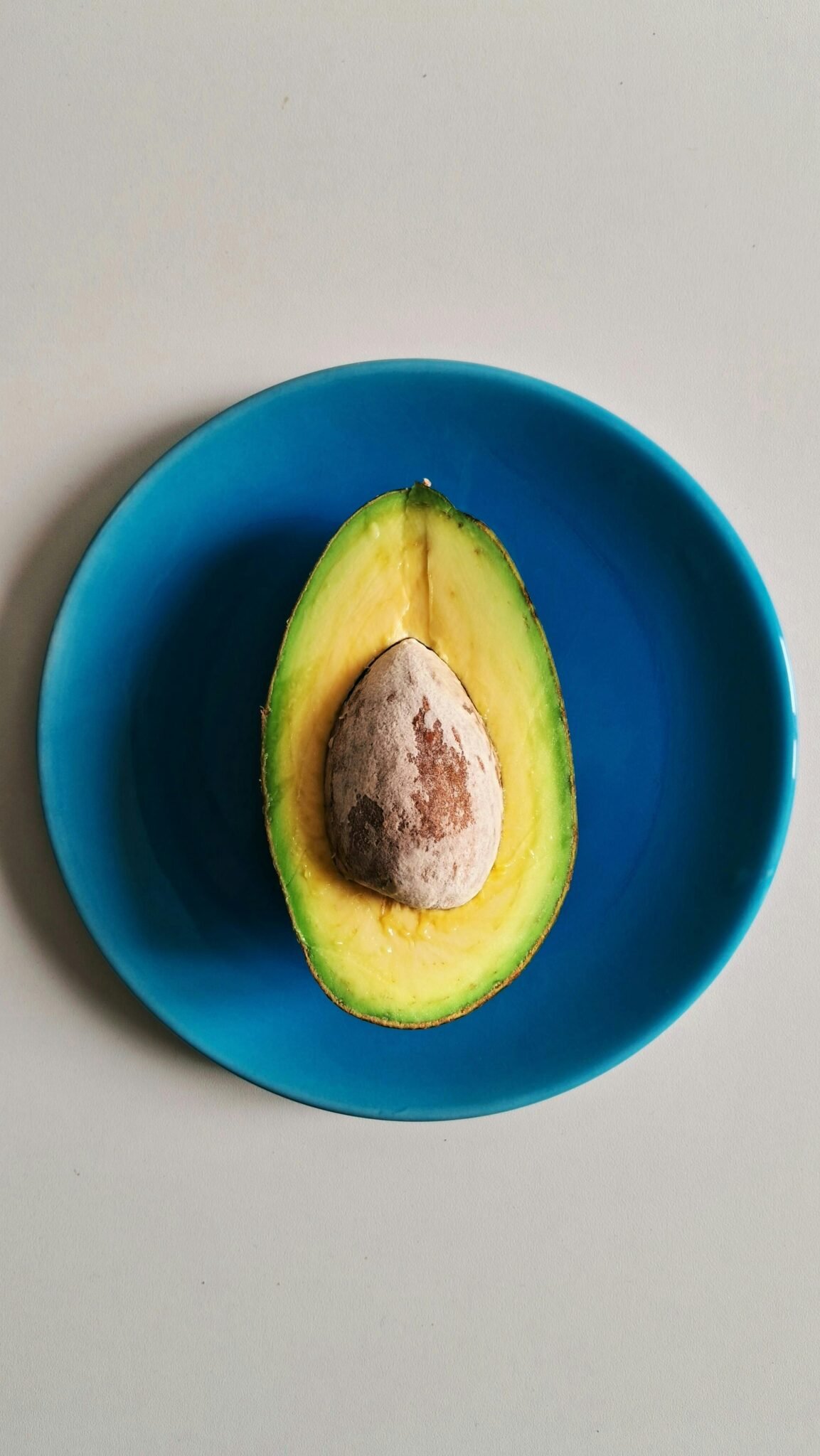A fresh avocado half with seed on a blue plate, perfect for health and food themes.